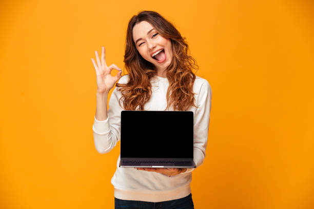 istock Cheerful brunette woman in sweater showing blank laptop computer screen 1279321752