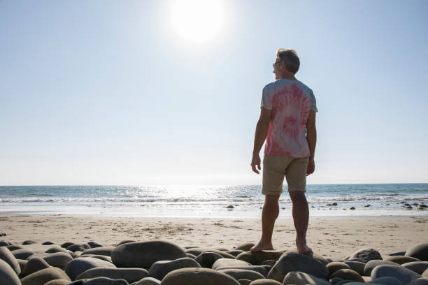 istock Mature man stands on boulders near beach edge 1279331092