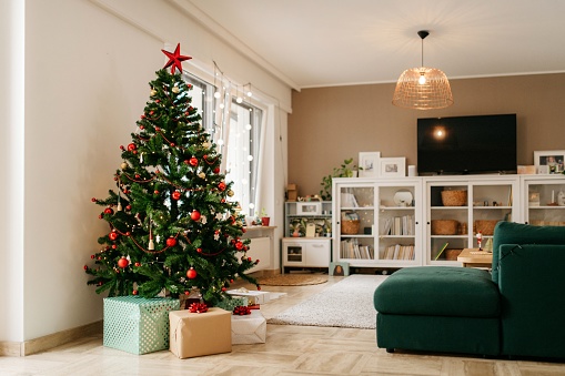 Decorated Christmas tree with gifts underneath. Wide angle photo with whole cosy living room visible. Christmas morning. No people. Daylight.