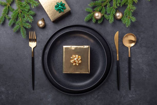 istock Christmas table setting. Black ceramic plate with golden gift box, fir tree branch and accessories on stone background. Gold decoration 1279335012