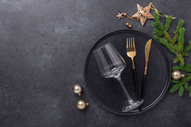 istock Christmas table setting with black ceramic plate, glass and gold decoration on black stone background. Top view. Copy space 1279335093