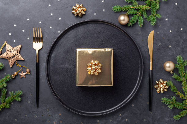 istock Christmas table setting. Black ceramic plate with golden gift box, fir tree branch and accessories on stone background. Gold decoration 1279335183