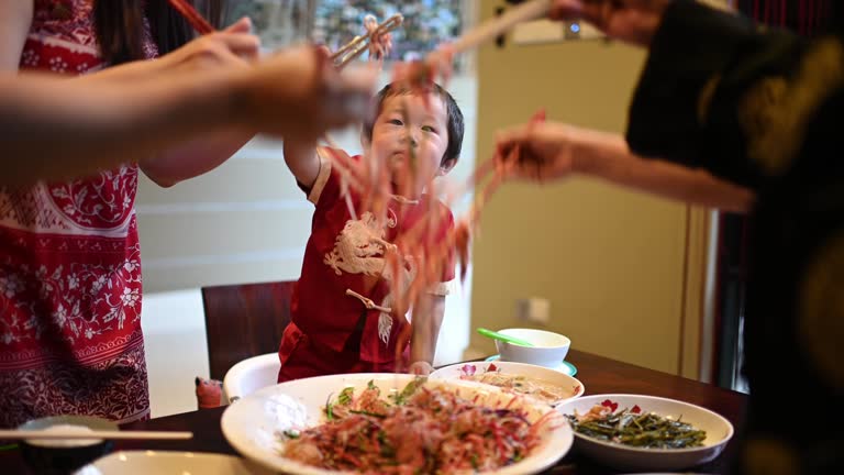 asian chinese family with traditional clothing celebrating chinese new year reunion dinner having traditional dishes raw fish lau sang symbolize prosperity, wealth and health