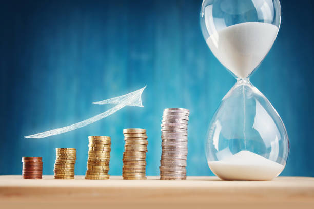 Clock with stacked coins and hourglass on blue background Clock with stacked coins. Pig with money savings and hourglass on blue background rigging stock pictures, royalty-free photos & images