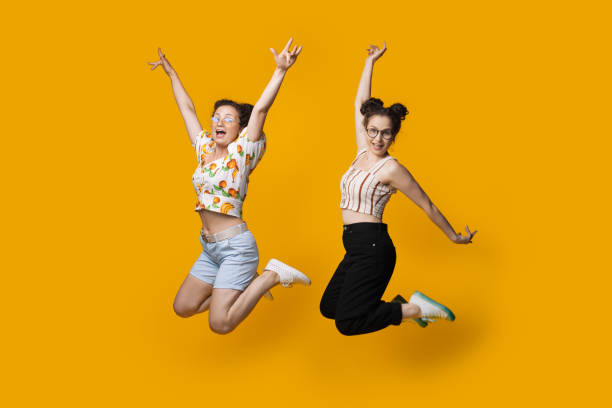 istock Caucasian twins jumping and gesturing happiness on a yellow studio wall while wearing summer clothes and glasses 1279341753