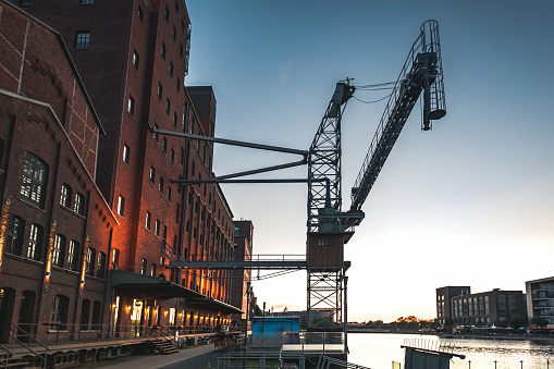 low angle view on old crane and buildings at the canal side of inner harbor in Duisburg at late summer evening