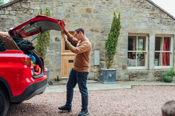Ready to Unpack A shot of a young man opening a car boot outside a country home ready to unpack. car trunk stock pictures, royalty-free photos & images