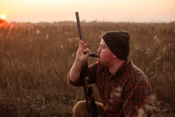 Photo of Young red bearded hunter  sitting it grass and blowing at hunter's whistle - photo with selective focus on his hand