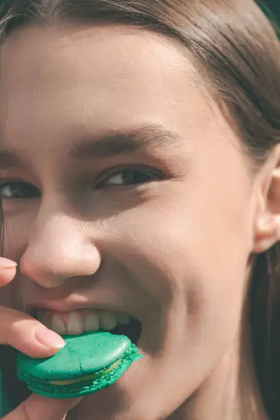 Portrait of young beautiful girl close-up, bites green macaroons