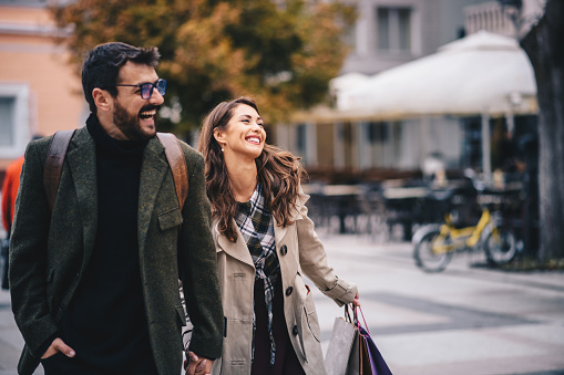 Young hipster couple walking down the street, smiling, enjoying on nice weather, holding their hands. Satisfied and relaxed, happy because of fine Autumn day.