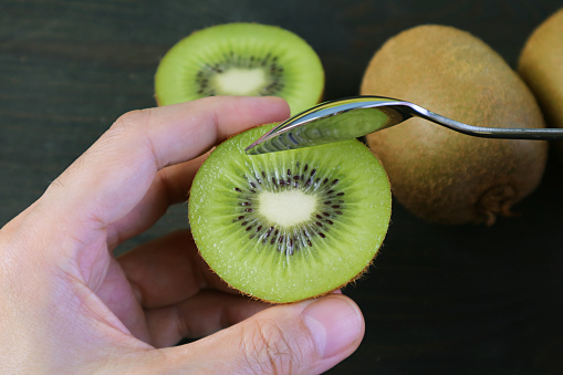 Closeup Hand Holding Cut Kiwifruit Scooping with a Spoon on Black Background