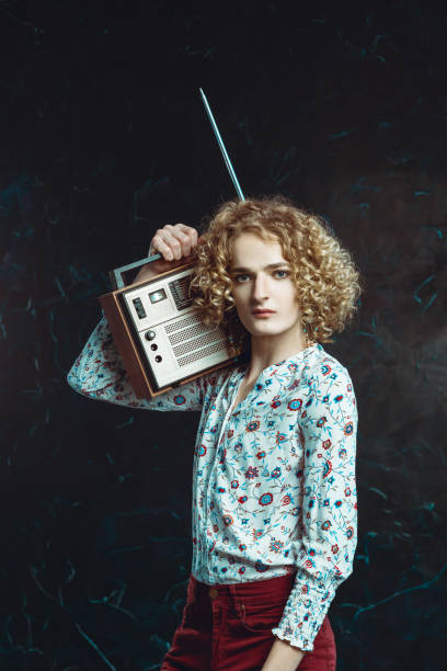 un jeune androgyne en chemise avec des fleurs écoute la radio sur une radio vintage. - radio show industry old old fashioned photos et images de collection