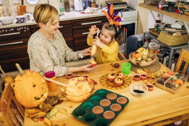 fille charmante aidant sa mère pour décorer des cupcakes d’halloween tout en utilisant une seringue avec le glaçage orange - coupe en dégradé photos et images de collection