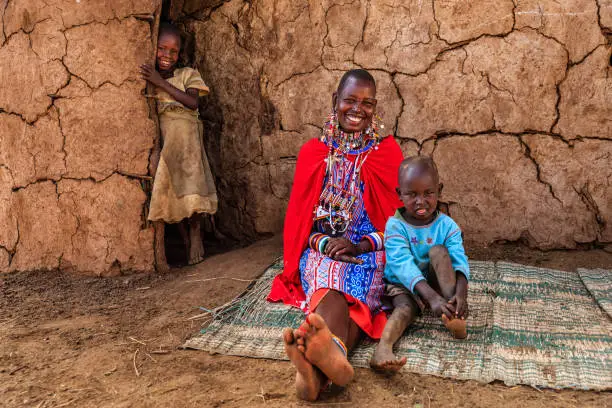 African mother from Maasai tribe sitting with her baby next to her hut, Kenya, Africa. Maasai tribe inhabiting southern Kenya and northern Tanzania, and they are related to the Samburu.