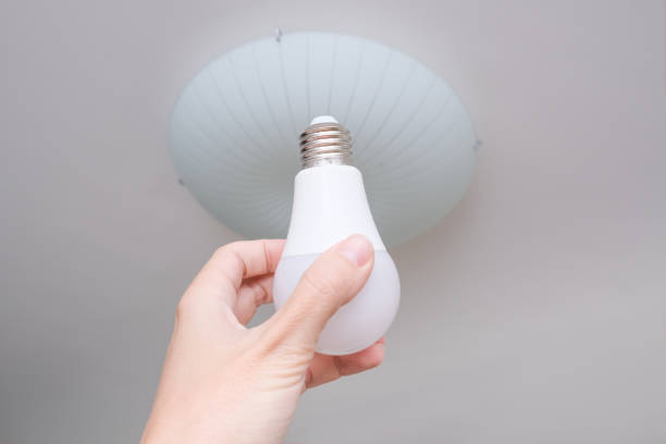 istock Female hand holding a led light bulb to change, replace it at home, screwing in the bulb into a lamp holder for energy saving and economy, saving money 1279366935
