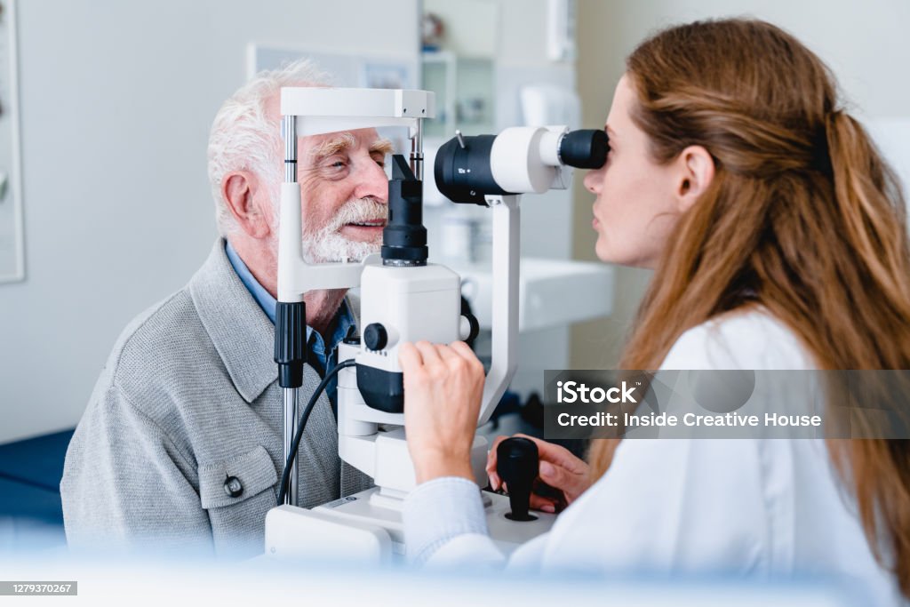 Female ophthalmic doctor diagnosing elderly patient`s sight using ophthalmic equipment Eye Exam Stock Photo