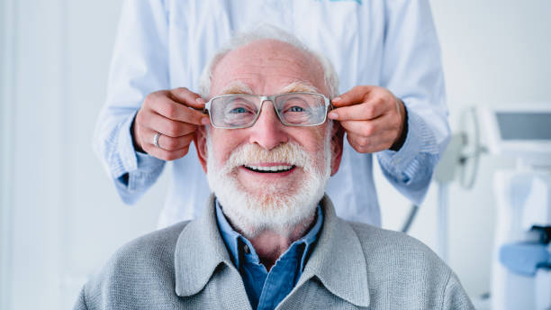 Doctor fitting glasses on cheerful aged male patient: cropped photo stock photo