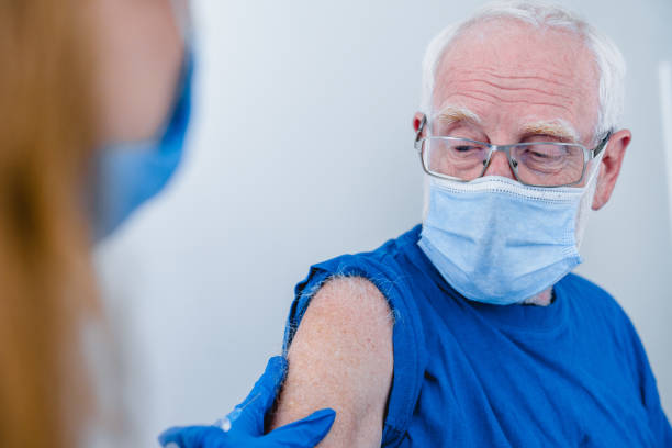 nahaufnahme foto von senior mann arm mit arzt hände machen injektion. älterer patient trägt maske, um die ausbreitung des coronavirus zu stoppen - isolated cold virus head and shoulders cold and flu stock-fotos und bilder