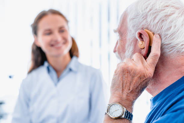 Focused picture of an elderly male patient with hearing aid side view with blurred woman doctor in the background Focused picture of an elderly male patient with hearing aid side view with blurred woman doctor in the background audiologist stock pictures, royalty-free photos & images