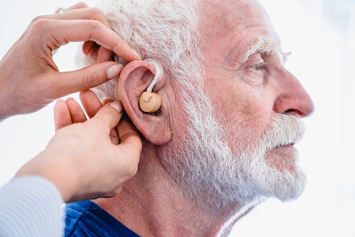 Side view of male senior patient with hearing aid being installed by doctor isolated over white background