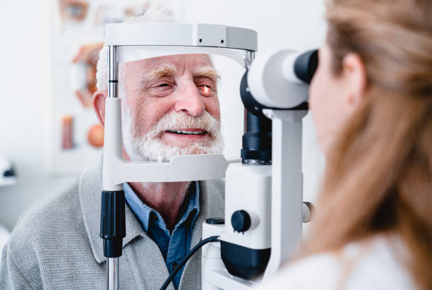 patient âgé gai de sourire étant vérifié sur l’oeil par le docteur ophtalmique féminin - examen ophtalmologique photos et images de collection