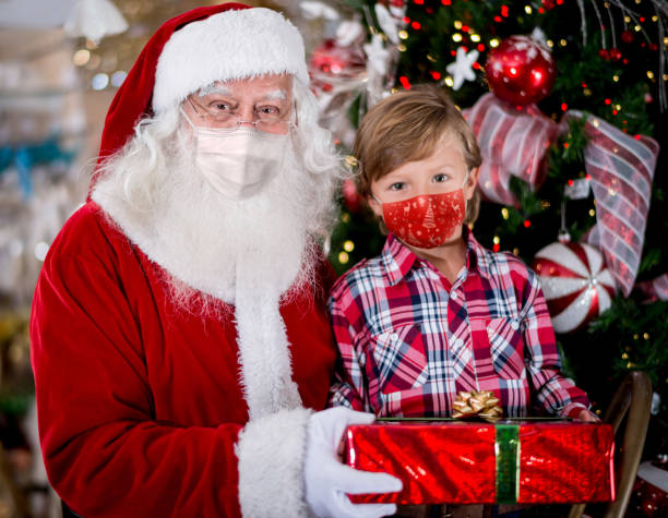 Portrait of a little boy with Santa wearing facemasks while getting a gift