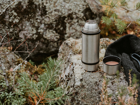 thermos flask outdoors in nature forest outdoors activity adventure hot chocolate\nPhoto taken outdoors in sunlight in forest with moss and stone