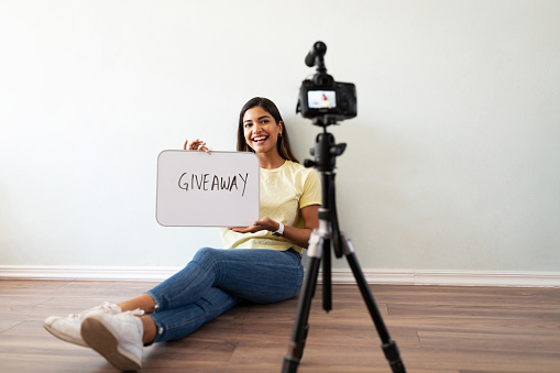 Portrait of a Hispanic influencer holding a sign and announcing a product giveaway to her social media audience