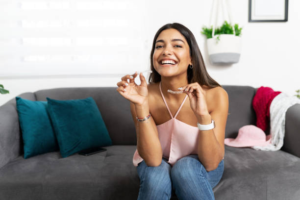 Cute woman happy about dental treatment Portrait of a beautiful Hispanic woman looking happy and smiling while holding a couple of dental retainers for her orthodontics treatment orthodontist photos stock pictures, royalty-free photos & images