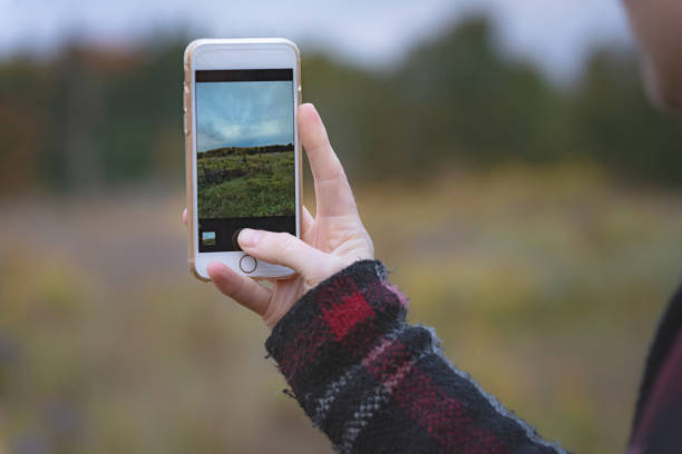 Person taking a picture of an autumn field. Blurred background with focus on the hand and phone.