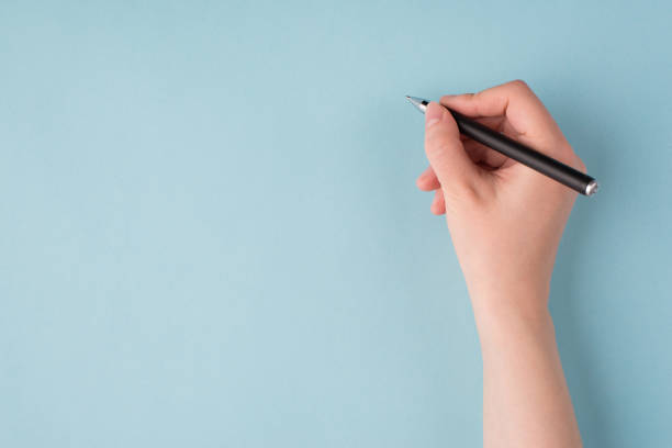 상단 위에 닫기 소녀의 오른손은 파란색 파스텔 배경에 고립 된 쓰기 시작 검은 펜을 들고 있는 소녀의 오른손의 사진을 닫습니다 - letter writing handwriting human hand 뉴스 사진 이미지