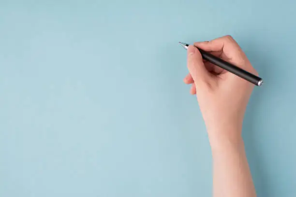 Photo of Top above overhead close up first person view photo of girl's right hand holding black pen starting to write isolated over blue color pastel background