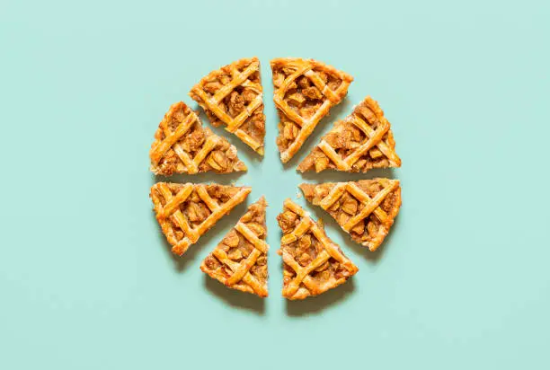 Apple pie cut into slices, isolated on green-mint seamless background. Flat lay with homemade apple pie slices. Traditional tart with a lattice crust.