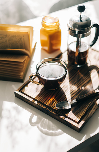 Coffee brewed in a French press and a cup on a wooden board with open book on a table. Morning at home, coziness and comfort. High quality photo