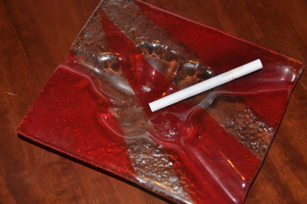 cigarette in red glass ashtray on brown closeup