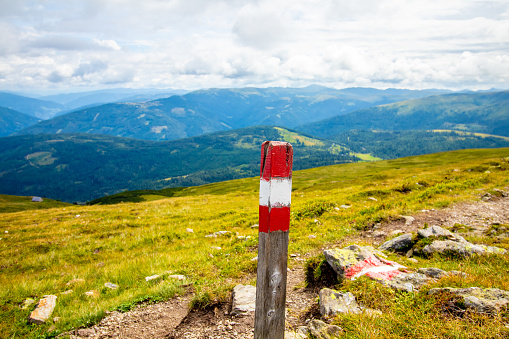 A wooden hiking marker painted in the colours of the Austrian flag showing the way on the plateau of the Aineck in the Austrian Alps.