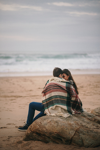 Rear view of a young couple with autumn/winter clothing sitting at the beach