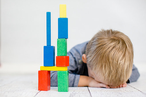 child lies with his head on the floor next to him is a wooden tower