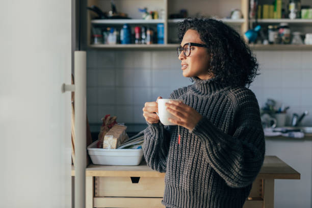 gesunde morgengewohnheiten: eine junge frau trinkt heißen tee in der küche - tee warmes getränk stock-fotos und bilder
