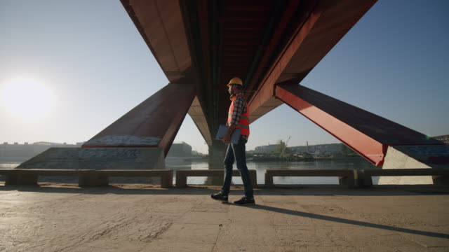 Architect with a laptop walks under a bridge on a construction site