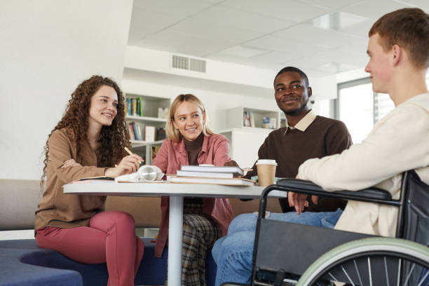 Diverse Group of Students in Library Low angle view at multi-ethnic group of students studying in college library featuring young man using wheelchair in foreground physical disability photos stock pictures, royalty-free photos & images