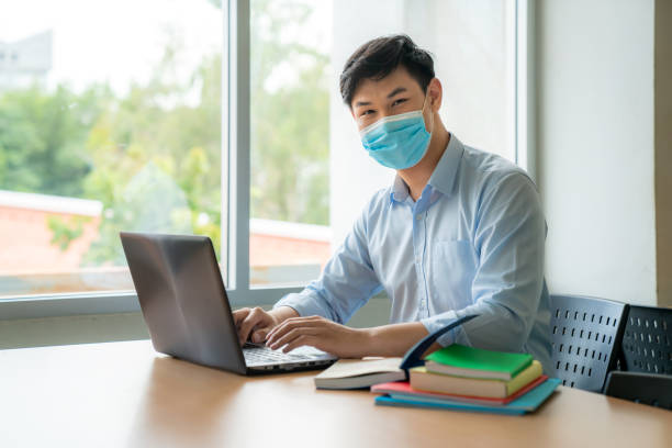 asian university student boy wearing face protective medical mask for protection from virus disease working with laptop at college. education, high school, university, learning and people concept - medical student healthcare and medicine book education imagens e fotografias de stock