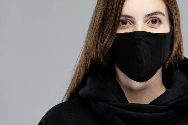 istock Young nice woman is posing with face mask. Studio portrait, concept with copy space. Gray background, isolated person in black clothing wearing facemask 1279414034