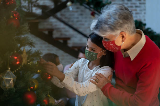 istock Girl and loving grandmother wearing facemasks while decorating the Christmas tree 1279421221