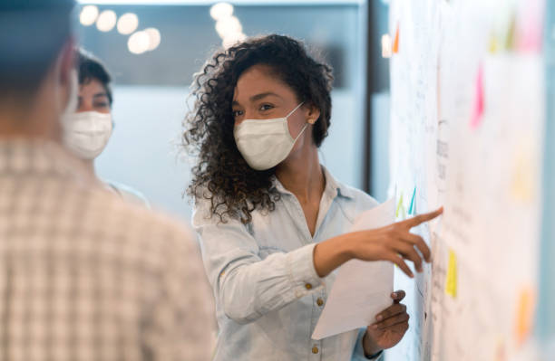 istock Woman sharing ideas with her team at a creative office while wearing facemasks 1279421242