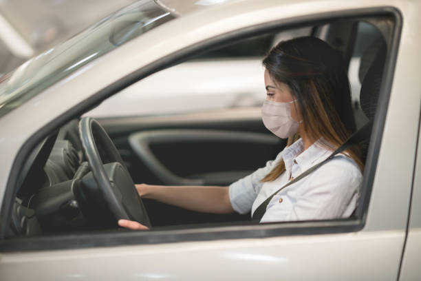 Woman wearing a facemask while driving a car at the dealership or the garage Woman wearing a facemask while driving a car at the dealership or the garage - pandemic lifestyle concepts car rental covid stock pictures, royalty-free photos & images