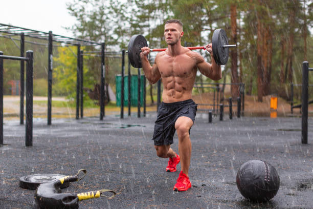 Full length photo of a man doing exercise lunges outdoors on a rainy day Full length photo of a man doing exercise lunges outdoors on a rainy day. Outdoor workout under rain. bodybuilder lunge