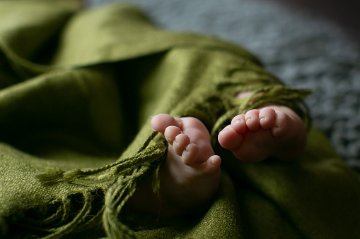 A close up of a new born baby's feet wrapped in a green blanket with soft light.