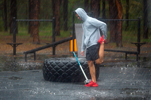 A man stretches his legs before a hard workout. A hard outside training ina a rainy day.