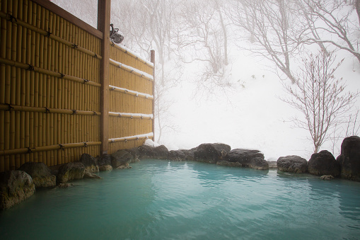A rotenburo onsen or outdoor hot spring bath with a view of trees and lots of snow in the mountains of Fukushima. The milky blue color of the water has beneficial health properties and a very low PH level. It also has a strong smell of sulphur.